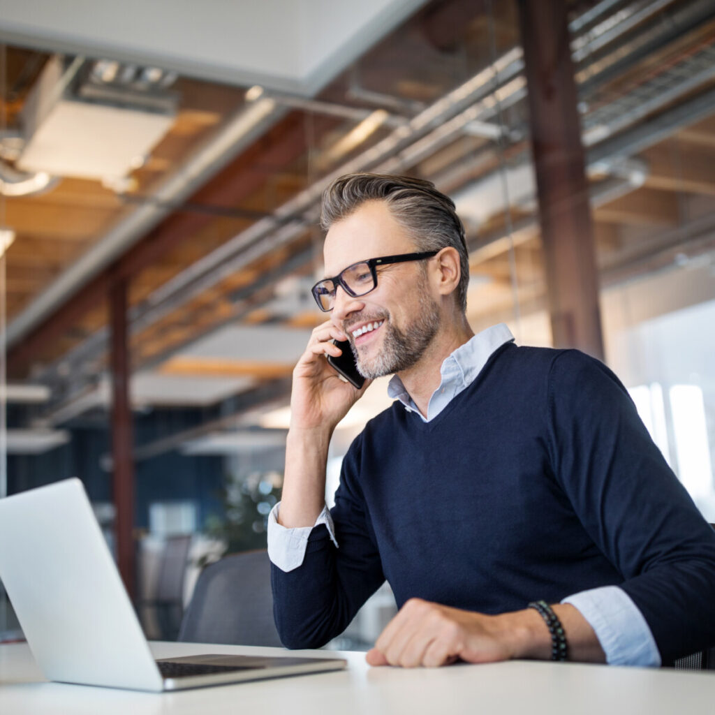 A business professional sitting at table with laptop and talking on mobile phone.