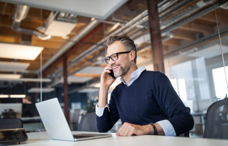 Mid adult business professional sitting at table with laptop and talking on mobile phone.