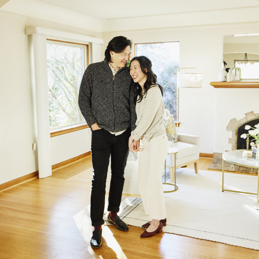 A smiling and embracing couple standing in living room of home for sale during open house.