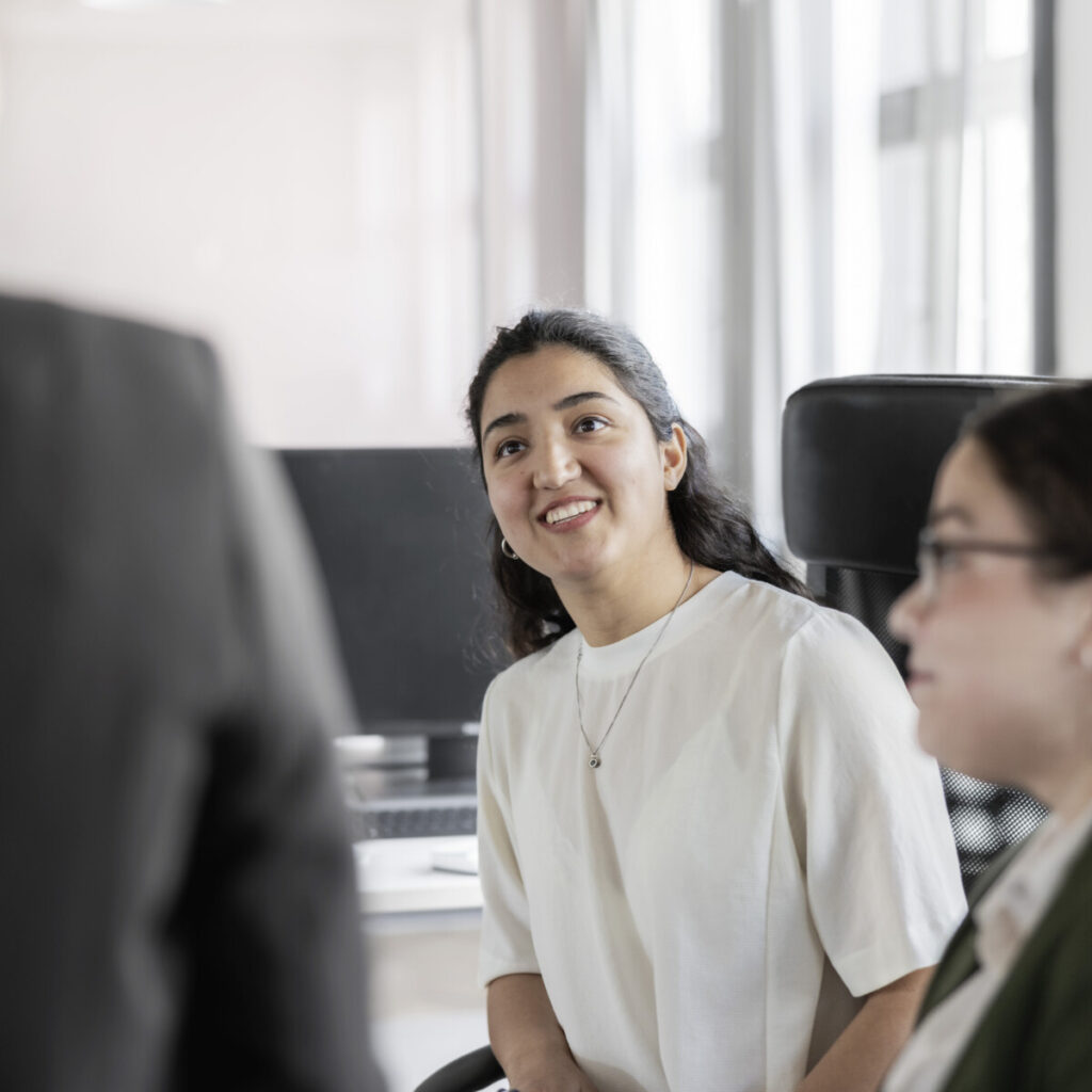 A happy young woman talking with colleagues in office.