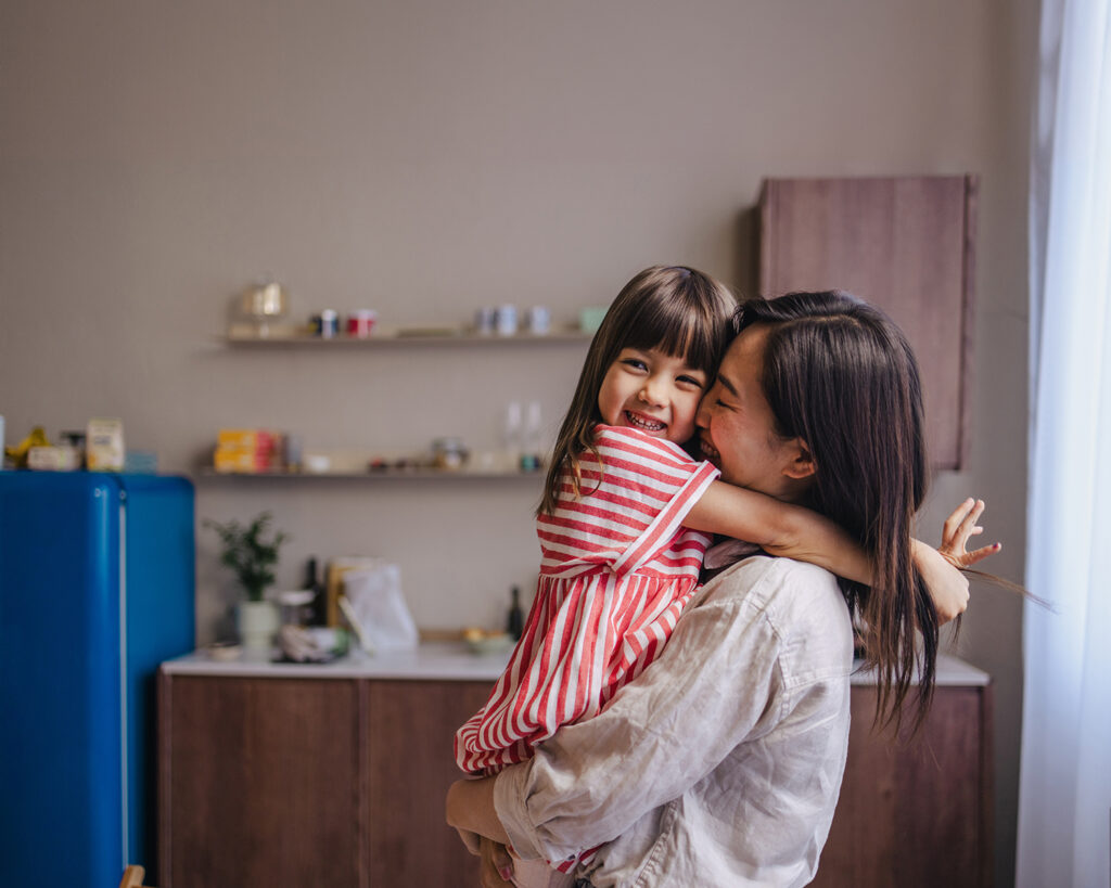 A mother happily holding a child in a kitchen of a house.