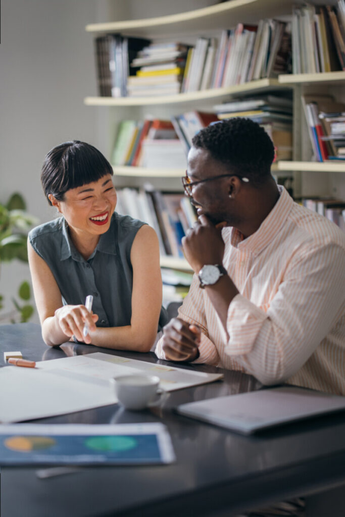 Two happy colleagues talking while working together in the office.