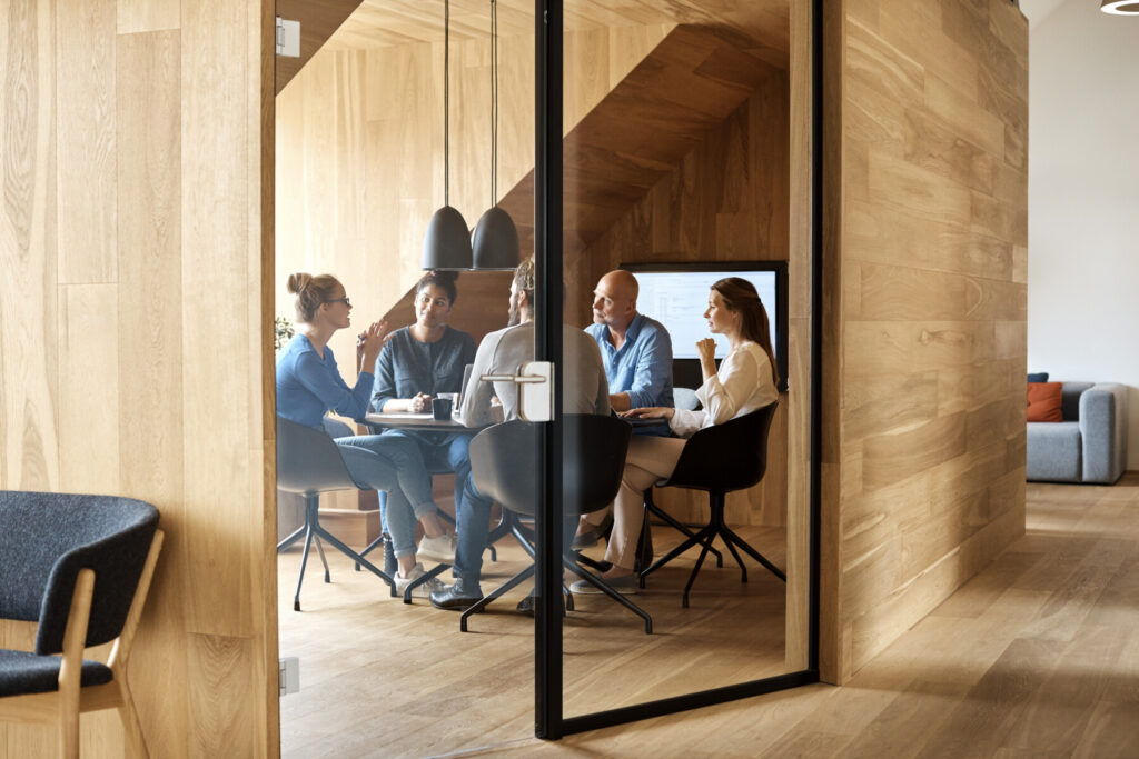 Business professionals discussing in meeting seen through glass door at office.
