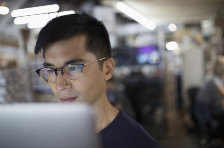 A man in glasses looking at a computer screen.