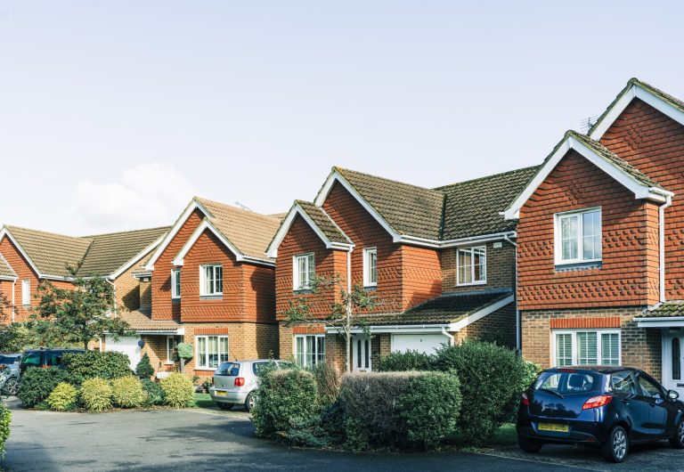 A row of brick houses with cars parked in front of them.