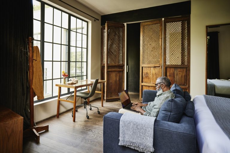 A real estate investor reviewing rental income documents on a laptop in a modern apartment unit.