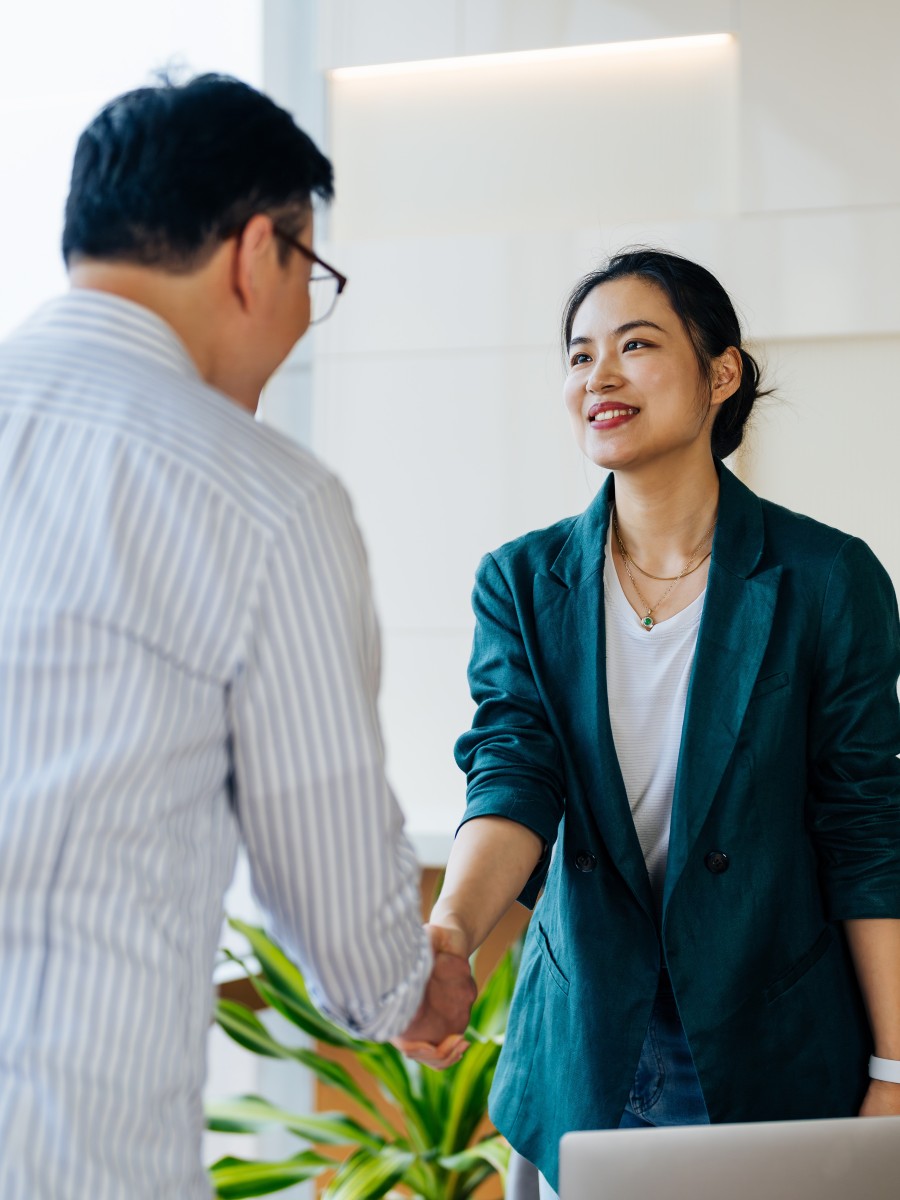 Cheerful Asian businesswomen shaking hands at office meeting.