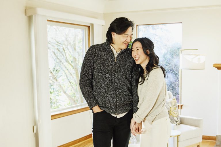 A smiling and embracing couple standing in living room of home for sale during open house.