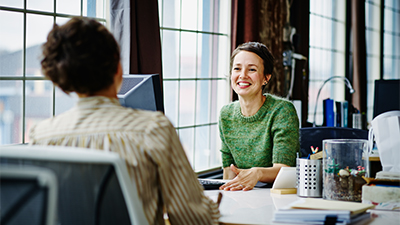 A smiling female business owner in discussion at workstation in office