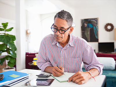 A mature man with glasses reviewing financial documents at home, managing personal business finances