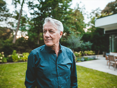 A senior man with white hair standing at backyard