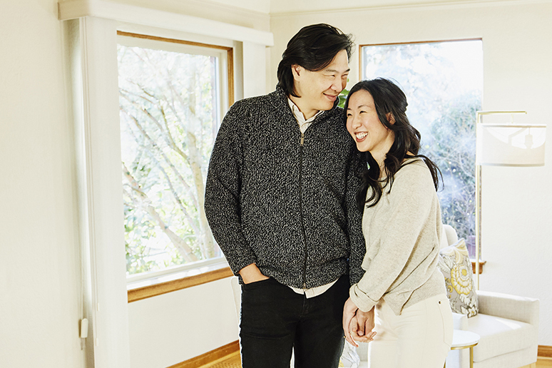 A smiling and embracing couple standing in the living room of home for sale during open house.