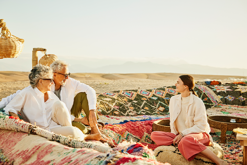 Smiling senior parents relaxing with their adult daughter while enjoying sunset at a desert camp during family vacation