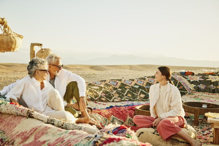 Smiling senior parents relaxing with their adult daughter while enjoying sunset at a desert camp during family vacation