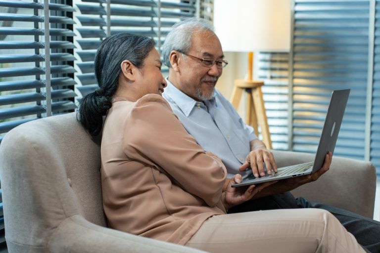 An Asian grandmother and grandfather smiling as they video call their grandchild overseas