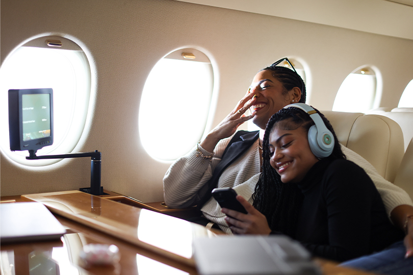 A mother and daughter laughing together while cuddling on a private jet
