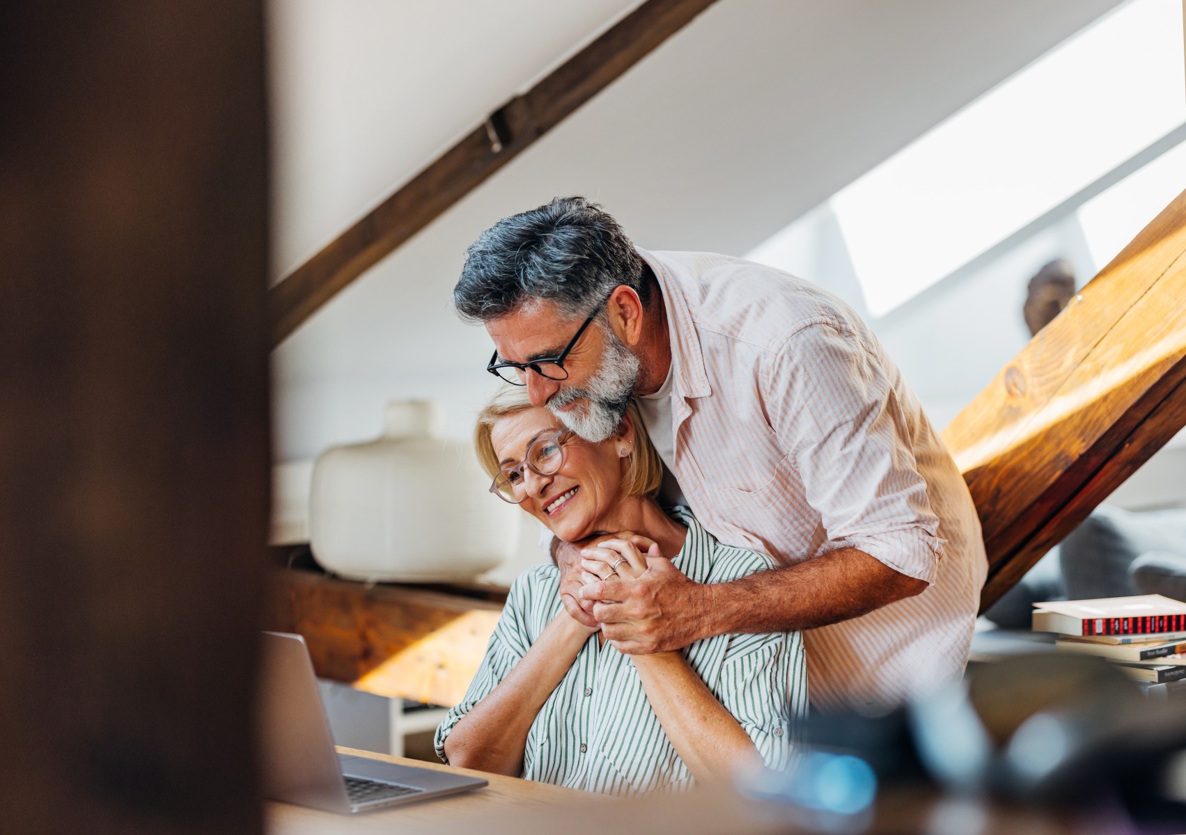 A couple lovingly embracing and smiling while using their laptop in their living room
