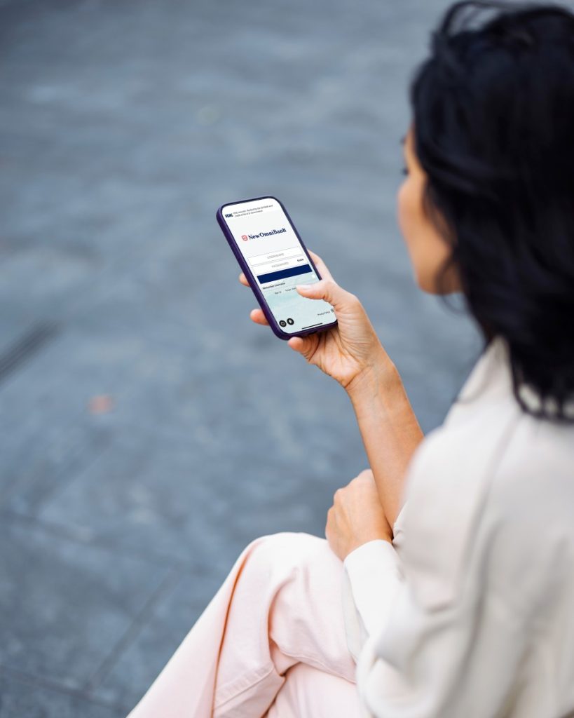 A businesswoman holding a cellphone that shows the login page of New Omni Bank’s banking app.