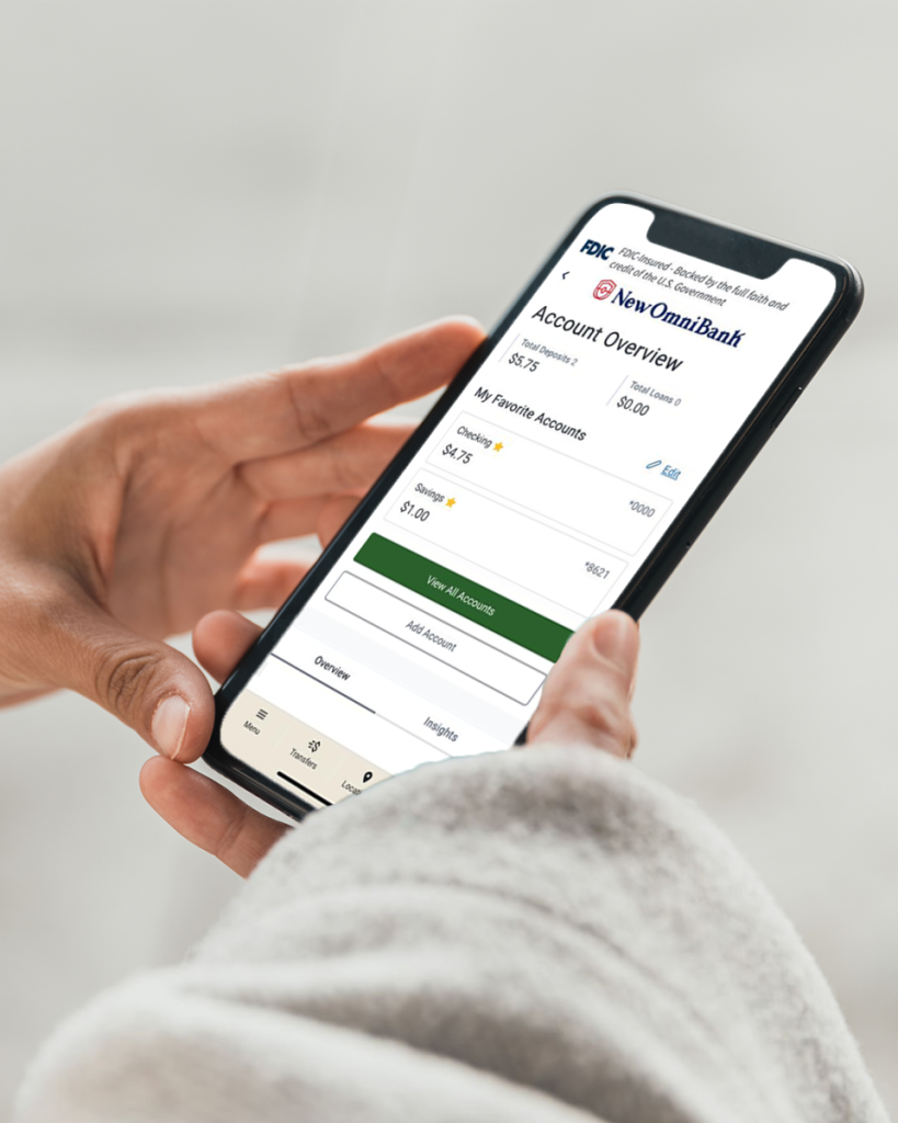 A hand holding a cellphone that shows the dashboard page of New Omni Bank’s banking app.