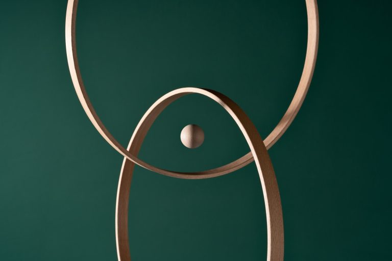 A wooden sphere in the center of intersected rings against a deep green background