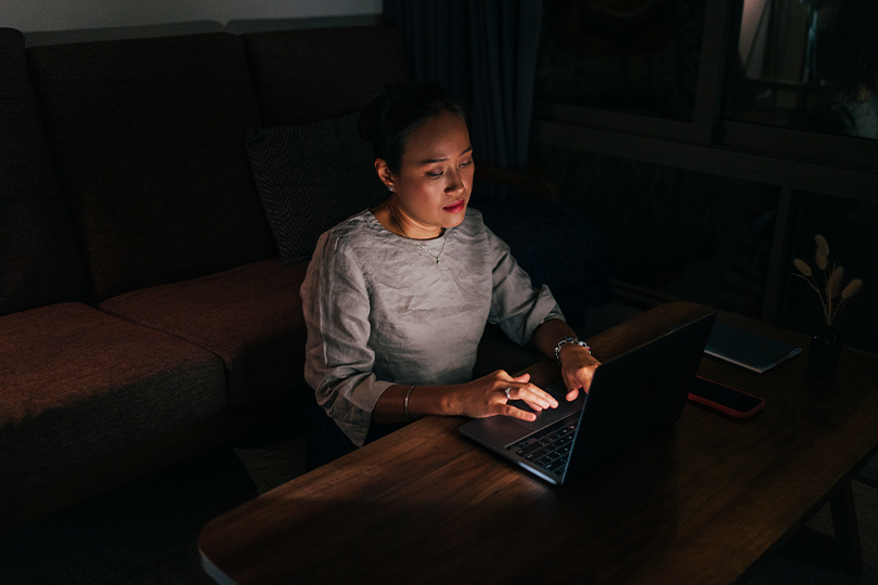 A woman sitting at home looking thoughtfully at her laptop screen, representing a cautious approach to online financial requests.