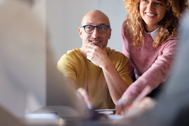 A business owner and an employee smile while reviewing work together at an office desk.