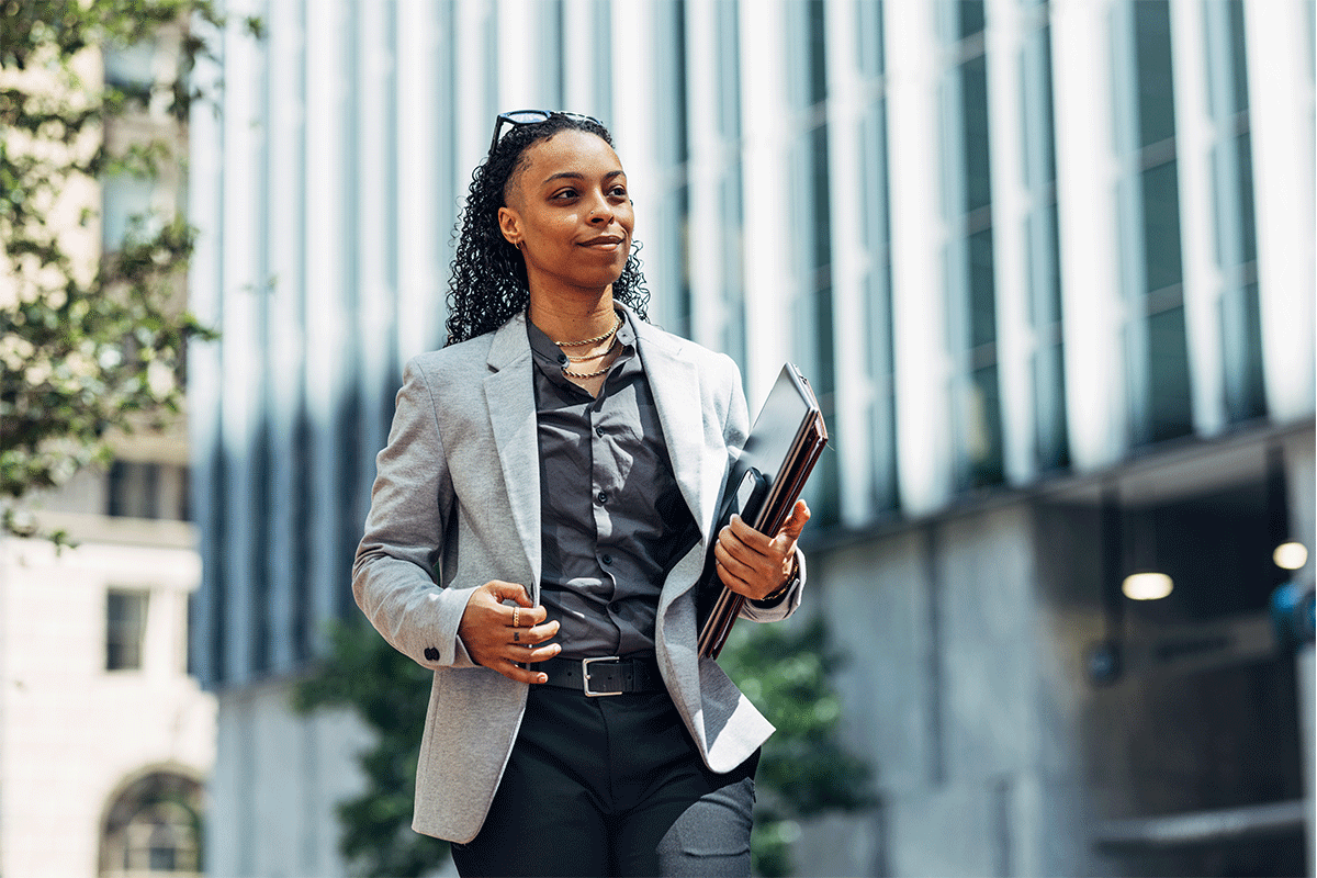 A confident businesswoman in formal attire walking outdoors in the city while holding documents, representing professionalism, ambition, and success
