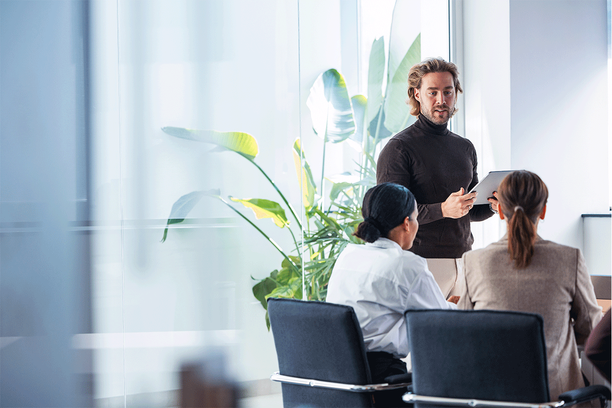 A focused speaker stands in front of two colleagues during a business meeting in a bright office